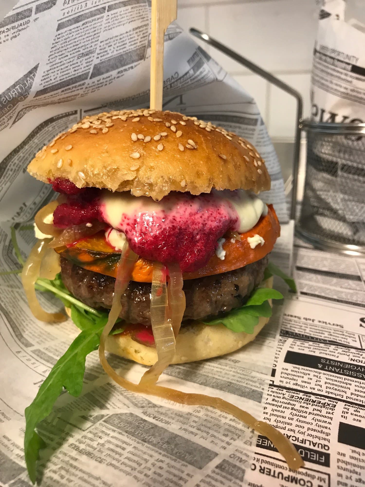 Burger im Sesam-Bun mit Patty, pinkfarbener Creme, einer orangefarbenen Gemüsescheibe und glasigen Zwiebeln auf Zeitungspapier